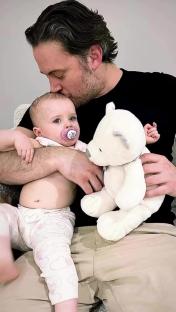 A man kisses his baby daughter, who is holding a teddy bear.