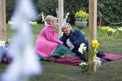 Two women sitting on a blanket in a garden.