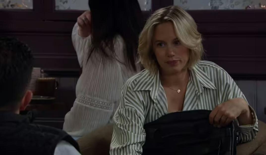 Screenshot of a woman in a striped shirt sitting with a handbag.