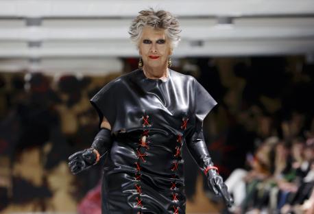 Prue Leith walking a runway in a black leather dress.