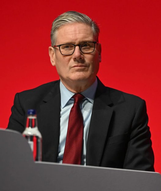Keir Starmer speaking at a podium against a red background.