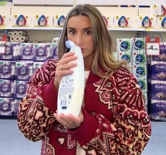 Woman in a red cardigan smelling a bottle of Dove body wash in a store.