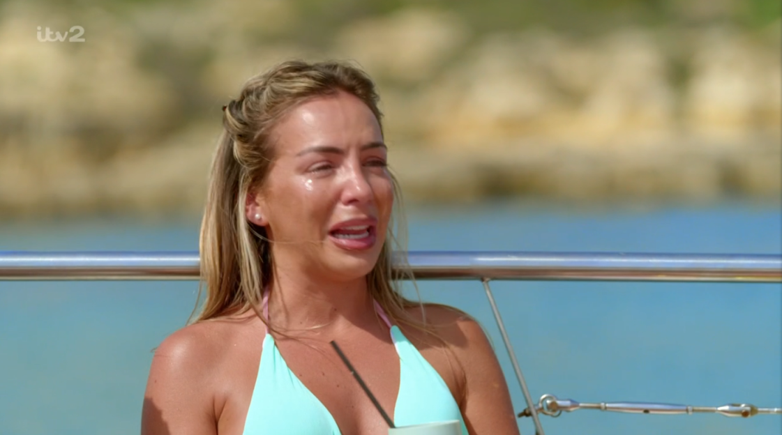 Woman in a teal bikini crying outdoors.