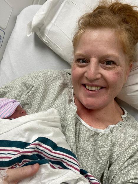 A smiling mother in a hospital gown holding her newborn baby.