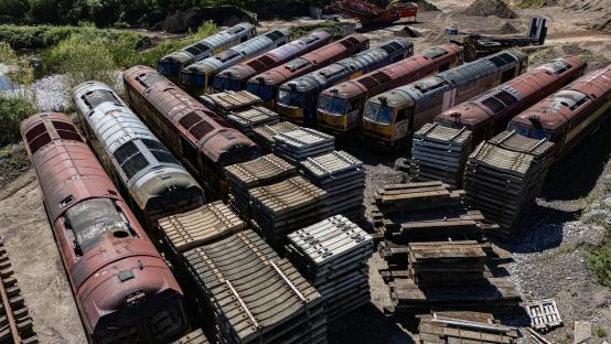 Aerial view of a dozen rusty diesel locomotives and railway sleepers in a quarry.