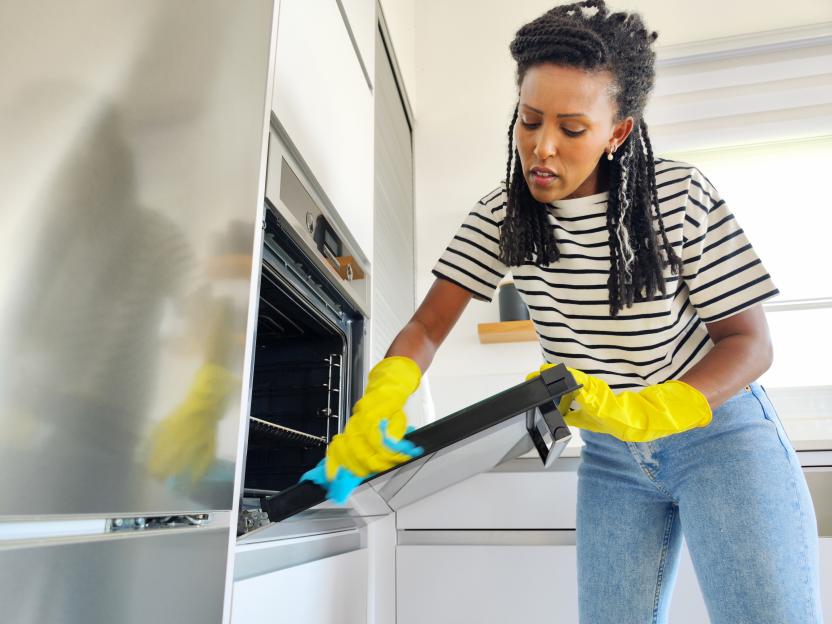 Woman in yellow gloves cleaning a kitchen oven.