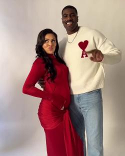 Pregnant woman in red dress and man in cream sweater.