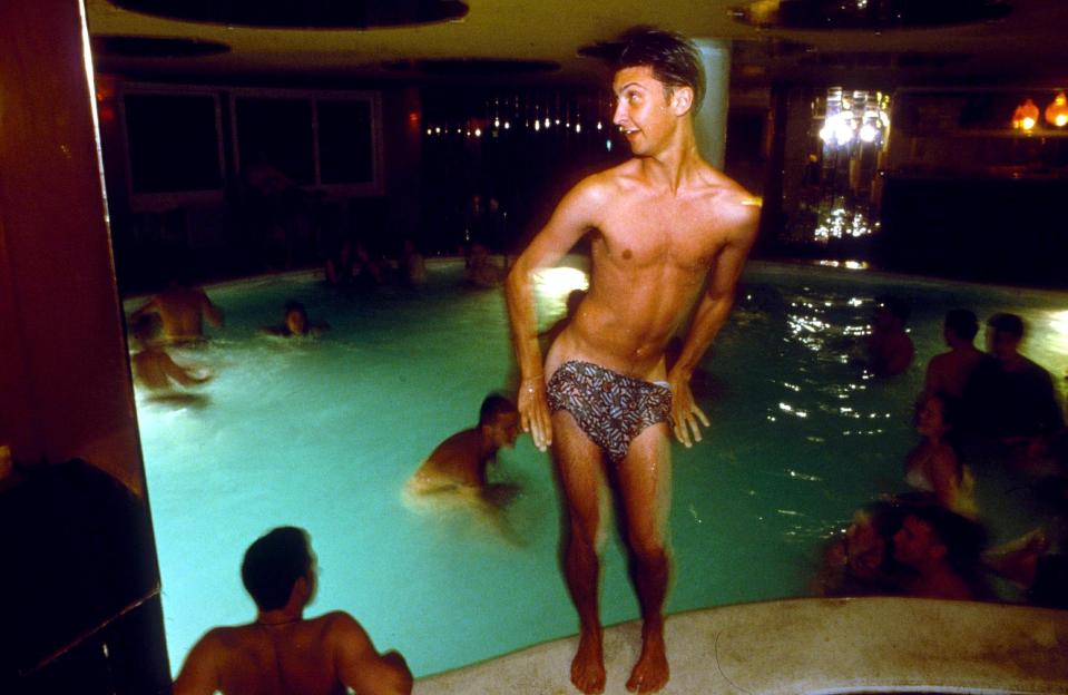 Photo of a naked man at a pool party partially covering his genitals.