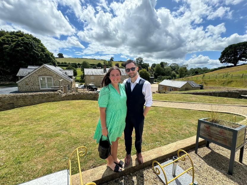 Portrait of a man and woman standing on a low wall in front of houses.