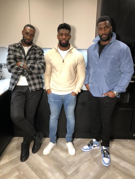 Three men standing in a kitchen.