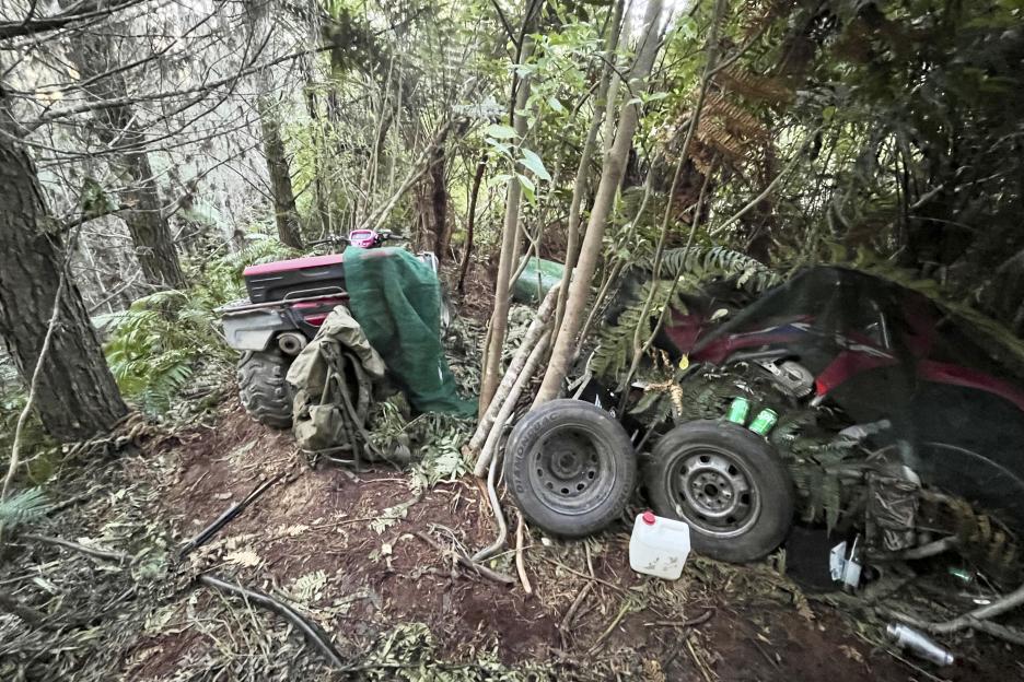 Photo of a campsite in a forest with two all-terrain vehicles and camping gear.