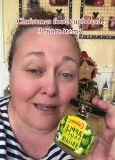 Woman holding a jar of Colman's apple sauce; Christmas food cupboard.