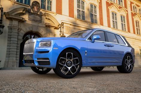 A blue Rolls-Royce Cullinan SUV parked in front of a building.