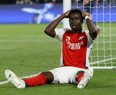 Bukayo Saka of Arsenal sitting on the field near the goal, looking dejected after missing a scoring opportunity.