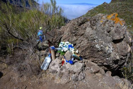 Memorial with flowers and water bottles near a rocky overlook.