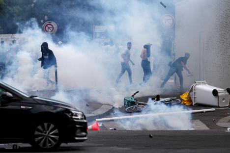 Individuals clashing with police officers amidst smoke and debris.