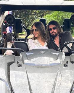 Liz Hurley, Billy Ray Cyrus, and their dog in a side-by-side vehicle.