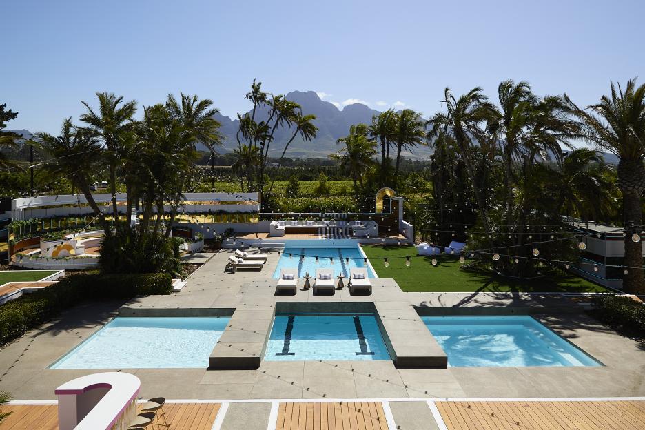 Love Island All Stars Villa, featuring multiple pools, palm trees, mountains, and string lights.