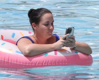 Woman in a pool using a smartphone while floating on a donut-shaped inflatable.