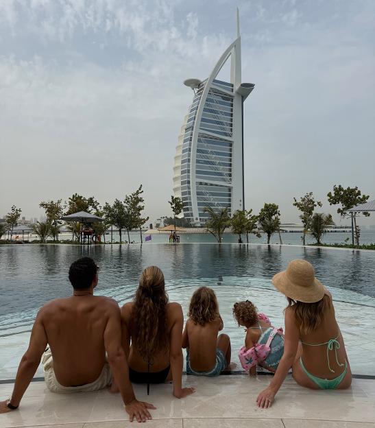 Family sitting by a pool with the Burj Al Arab in the background.