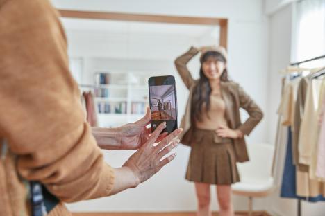A woman taking a photo of a young woman trying on clothes.