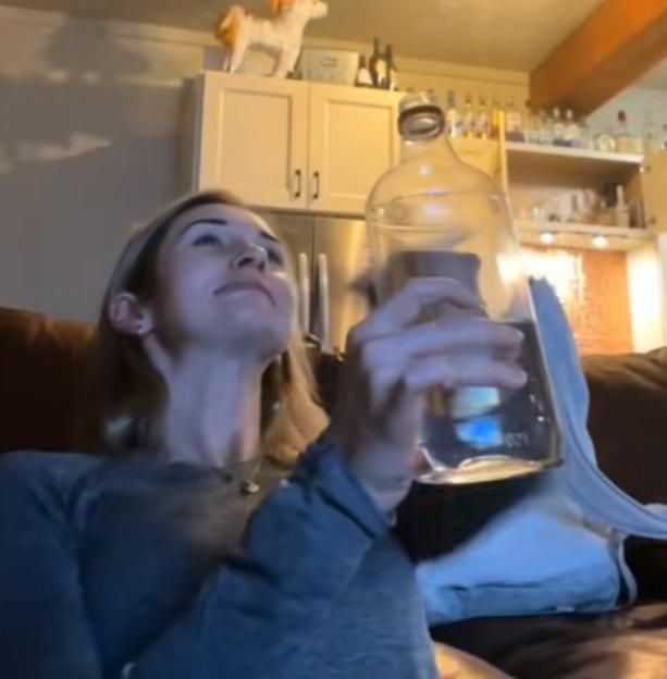 Woman holding a large glass bottle of alcohol.