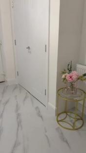 Hallway with white door, marble-look flooring, and gold side table with pink flowers.