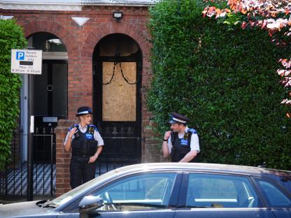 Two police officers standing outside a house with a boarded-up door after a suspected arson attack.