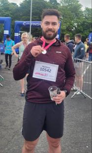 Man holding a medal and race bib after a race.