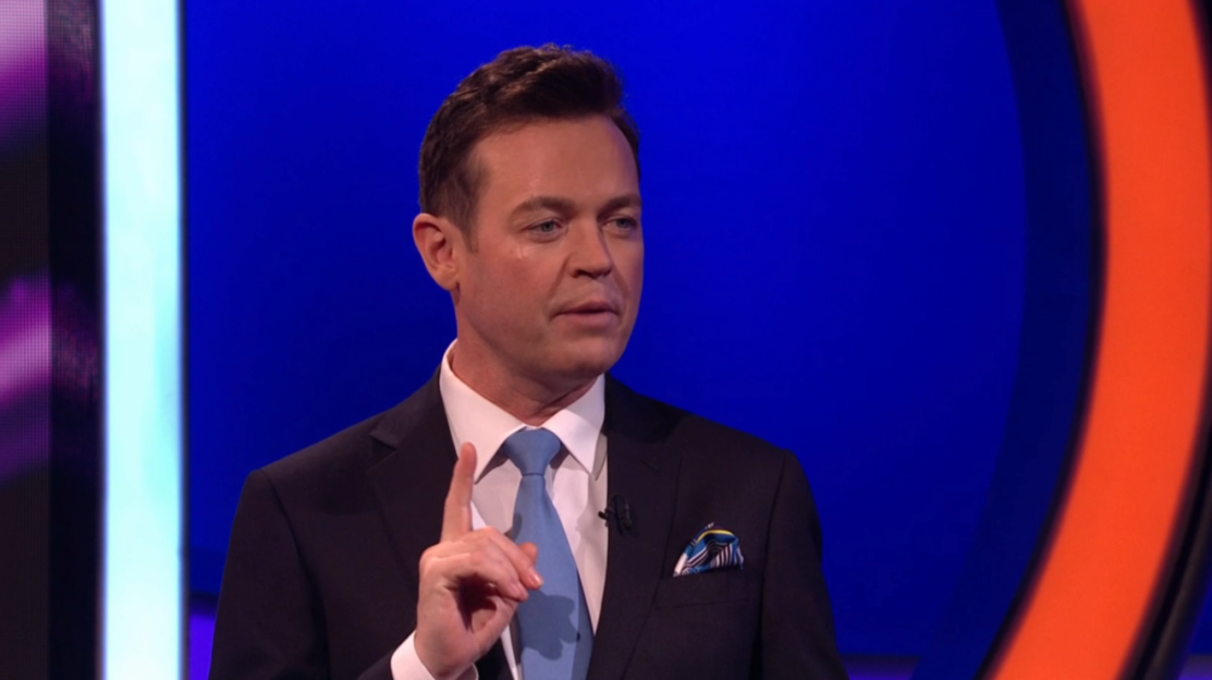 Man in suit speaking on television show.