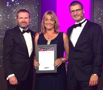 Woman receiving an Avon award with two other people.