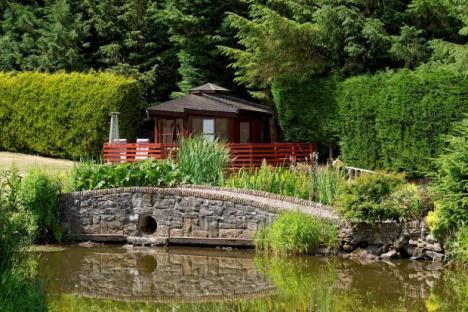 Stone bridge over a pond, with a small house and garden beyond.