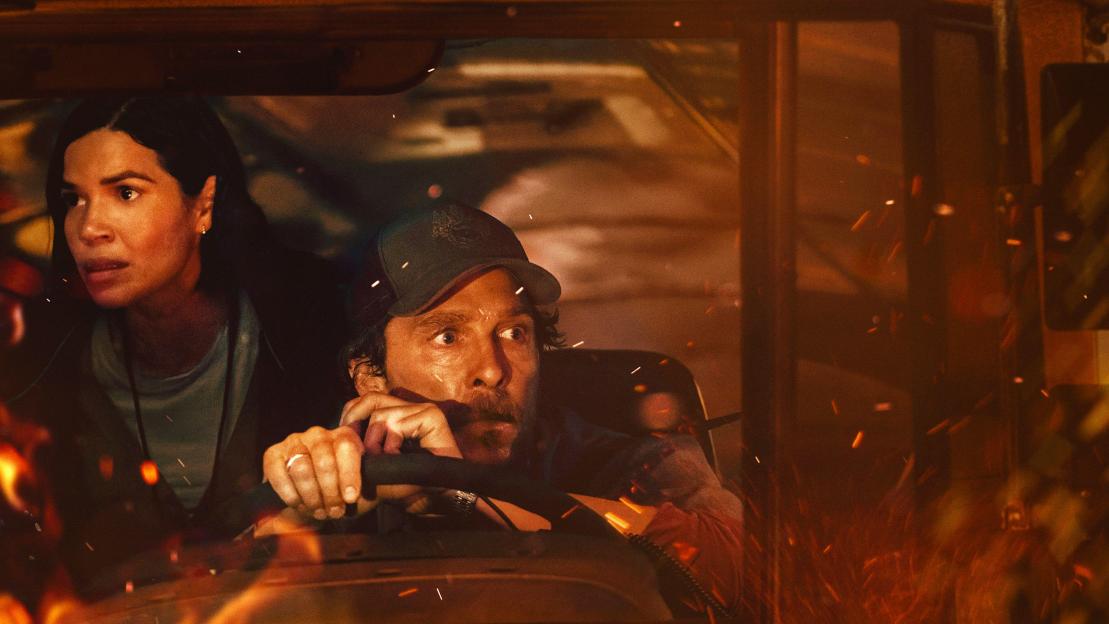 Matthew McConaughey and America Ferrera in a bus surrounded by fire, looking scared.