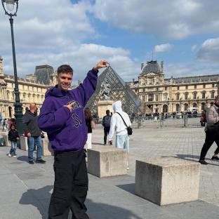 Romeo Beckham in Paris, gesturing towards the Louvre Pyramid.