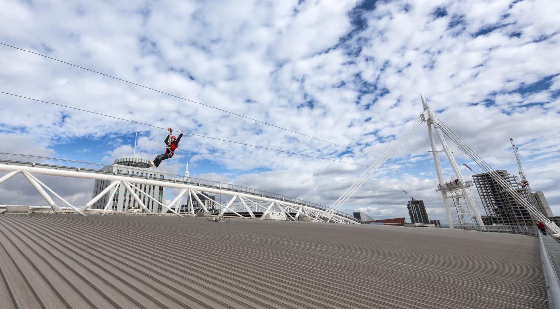 A person zip-lining over the roof of the Principality Stadium.