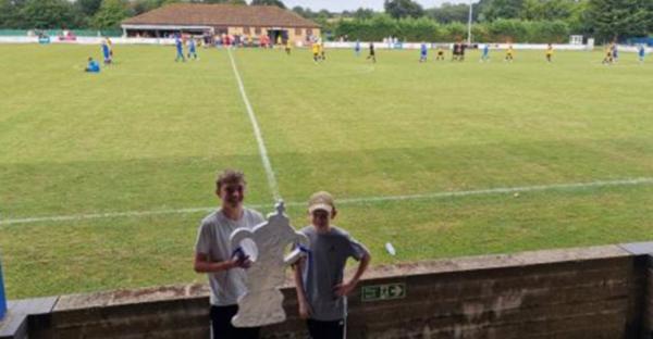 Two boys at a soccer game holding a model FA Cup trophy.