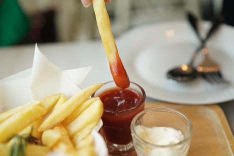 French fry being dipped in ketchup, with a side of mayonnaise and more fries.