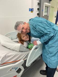 A man in scrubs hugs a young girl in a hospital bed.
