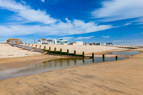 Houses on a beach with wooden groynes and a small stream.