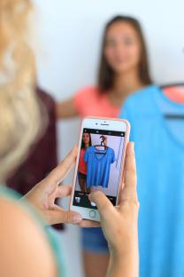 A person taking a photo of a blue shirt on a hanger with a smartphone.
