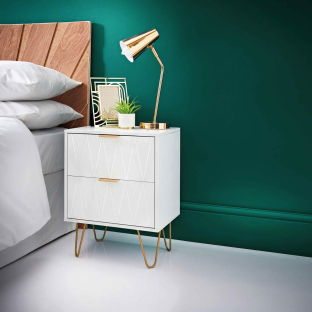 White bedside table with gold legs and accents, next to a bed.