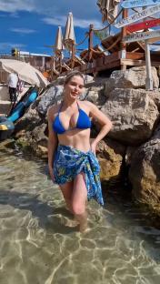 Woman in blue bikini and sarong wading in shallow water.