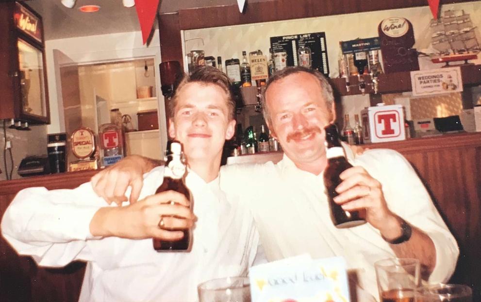 Photo of a young man and his father holding beers at a bar.
