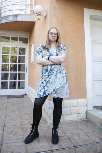 Woman in teal dress standing outside a house.