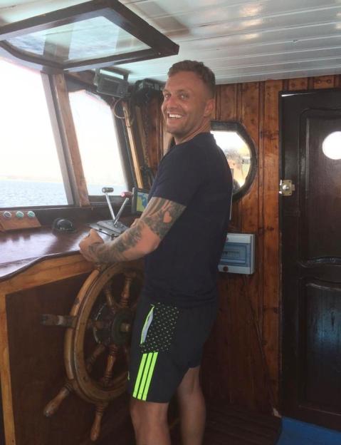 Man smiling at the helm of a boat.