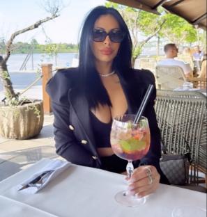 Woman sitting outdoors at a restaurant table, drinking a cocktail.