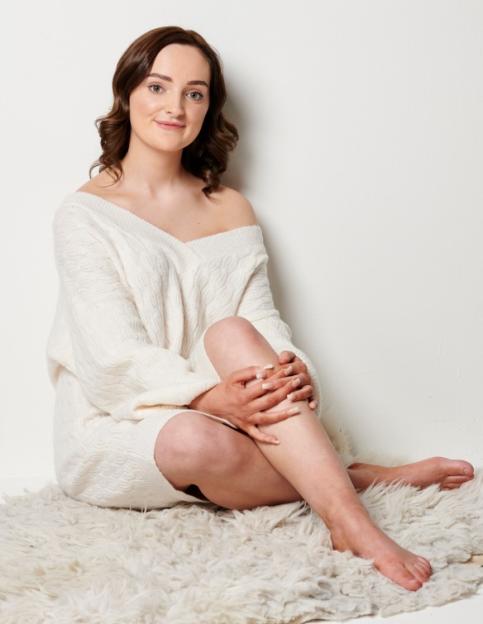 Woman in white sweater sitting on a fluffy rug.