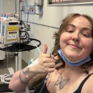 Woman giving thumbs up during cancer treatment.