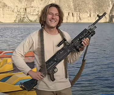 Man holding a machine gun by a body of water.