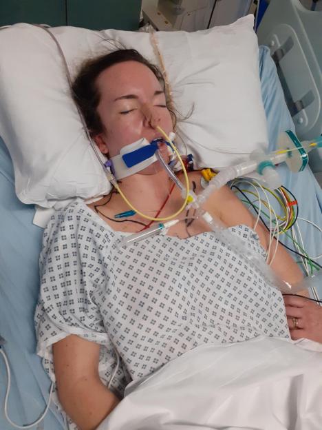 Woman in hospital bed with medical tubes.
